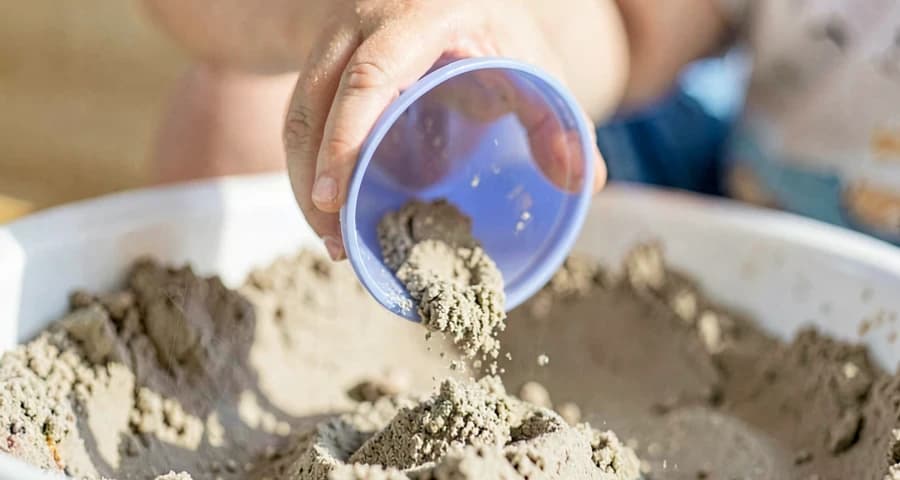 bebê despejando areia de um potinho durante atividade sensorial