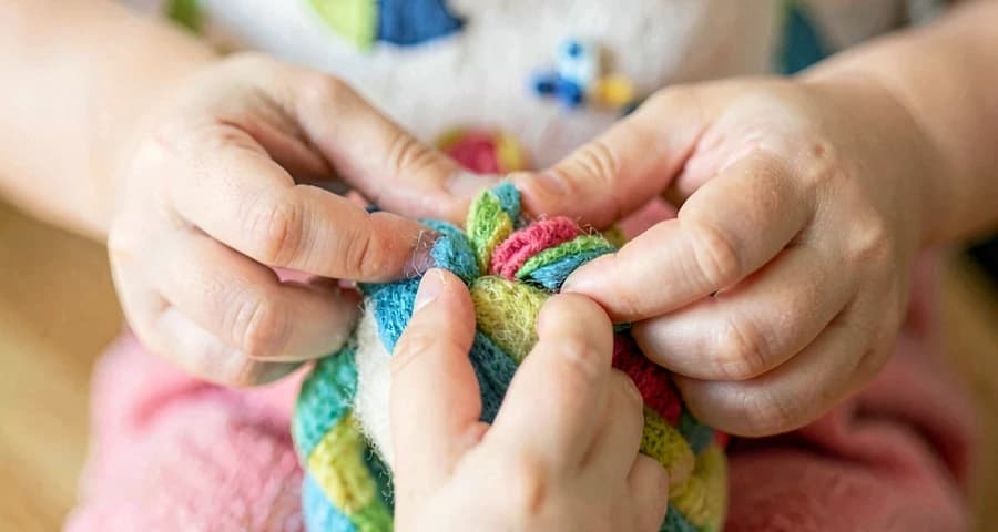 criança da creche montando boneca de tecido colorida em atividade de arte