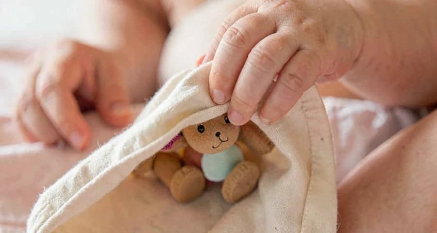 bebê descobrindo brinquedo escondido sob pano leve na creche