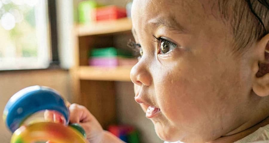 desenvolvimento sensorial bebê creche: rosto de bebê em foco observando som e movimento de instrumento musical