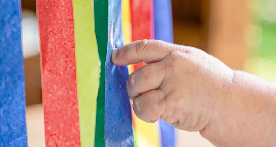 mão de bebê tocando tiras de papel coloridas penduradas na creche
