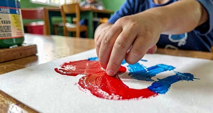 Marcas gráficas de bebê: detalhe de mão pequena deixando rastros coloridos em papel durante exploração sensorial com tinta