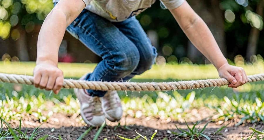 criança da creche pulando sobre corda esticada no chão durante atividade motora