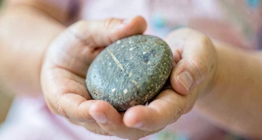 mão de bebê segurando pedra durante atividade sensorial de comparação na creche